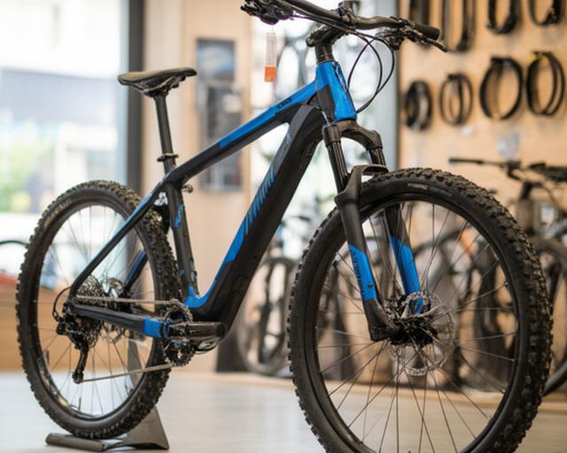 Bicicleta de montanha azul e preta exposta na loja com luz natural e acessórios pendurados na parede